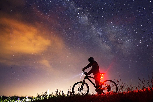 cyklist på cykel med lys med baggrund af stjernehimmel